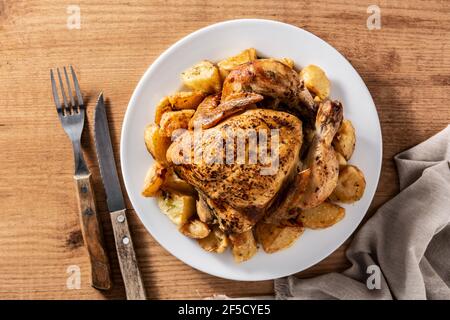 Pollo arrosto fatto in casa con patate su tavolo di legno Foto Stock