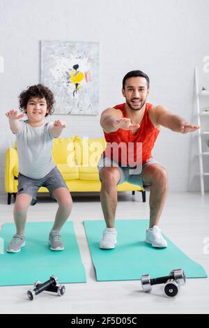 Ragazzo sorridente in abbigliamento sportivo facendo squadre vicino a padre arabo a. casa Foto Stock