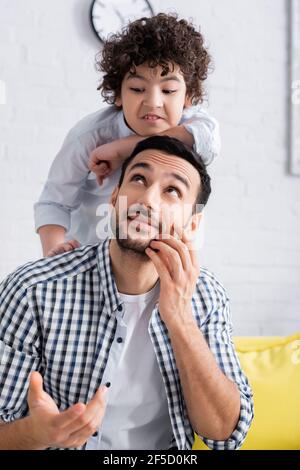 sorridente uomo arabo che punta con la mano mentre si guarda eccitato ragazzo a casa Foto Stock