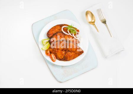 Friggitrice di pesce ben arrangiata e guarnita con cipolla, limone e pomodoro a fette su piatto bianco in ceramica posto su tavola blu cielo con texture bianca Foto Stock