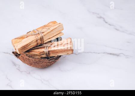 Palo Santo si stacca all'interno della conchiglia di cocco su sfondo di marmo chiaro - albero sacro dell'incenso dall'America Latina. Meditazione, salute mentale e personale Foto Stock