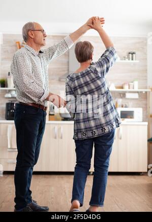 Gioioso vecchio e donna che danzano in cucina al mattino presto, rilassandosi dopo una sana colazione. Felice coppia anziana che ha divertimento, le persone in pensione in casa accogliente godendo la vita Foto Stock