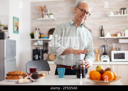 Uomo anziano che fa il caffè usando la pressa francese durante la prima colazione in cucina. Gli anziani al mattino gustano caffè marrone fresco, caffè espresso, caffeina da tazza d'epoca, filtro relax rinfresco Foto Stock