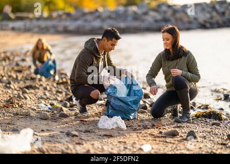 Team di volontari che lavorano duramente per raccogliere rifiuti di plastica in spiaggia Foto Stock