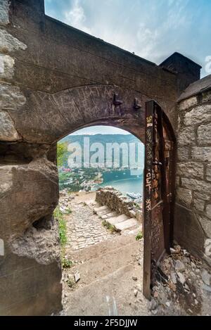 Una porta aperta storica ad arco della Fortezza di Cattaro incornicia una vista della baia sotto la collina. Foto Stock