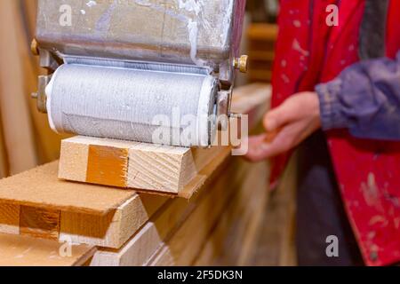 Primo piano su Falegnameria che utilizza un pratico utensile a rulli, spalmatore per applicare l'adesivo sui profili di superficie in legno che deve essere incollato. Foto Stock