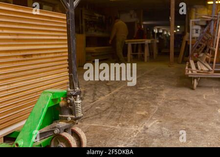 Transpallet manuale carico con sottili profili incollati disposti su di esso nel magazzino dell'officina del falegname. Foto Stock