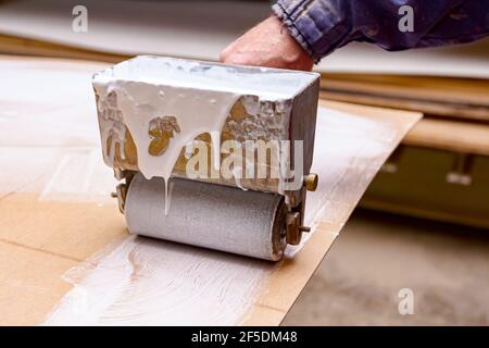 Primo piano sparato su carpenteria che utilizza un pratico utensile a rulli, spalmatore per l'applicazione di adesivo sul profilo di superficie in legno, compensato che deve essere g Foto Stock