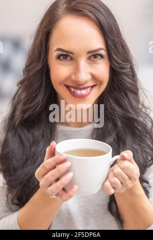 Giovane donna di brunetta che tiene una tazza di tè e odore delizioso aroma. Foto Stock