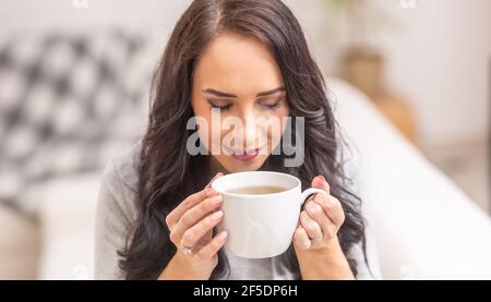 Giovane donna di brunetta che tiene una tazza di tè e odore delizioso aroma. Foto Stock