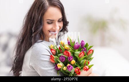 Felice donna dai capelli scuri che tiene un bel bouquet pieno di tulipani durante il giorno nazionale delle donne. Foto Stock