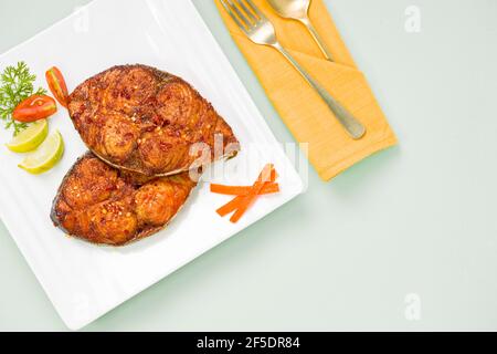 Friggitrice di pesce ben arrangiata e guarnita con fette di cipolla, limone e pomodoro su piastra in ceramica di forma quadrata bianca. Foto Stock