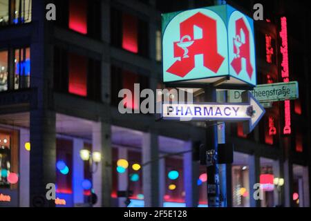 Berlino, Germania. 24 Marzo 2021. Un cartello al neon con il simbolo di una farmacia e una freccia illuminata con le parole 'Farmacia' si illuminano all'incrocio di Friedrichstraße e Dorotheenstraße di notte. A partire dalla settimana di calendario 14, i medici generici devono vaccinare contro COVID-19. I vaccini saranno distribuiti attraverso farmacie e grossisti farmaceutici. L'Unione federale delle associazioni dei farmacisti tedeschi e. V. (ABDA) informa le farmacie come procederà il processo di ordinazione e la consegna dei vaccini. Credit: Stefan Jaitner/dpa/Alamy Live News Foto Stock