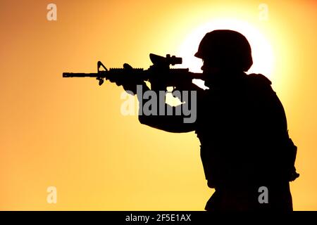 Silhouette di moderno soldato di fanteria dell'esercito in piedi sullo sfondo di impostare il sole e mirare fucile d'assalto con la vista collimatore. Operazioni speciali rifleman, sparatutto forze d'élite sparare in nemico Foto Stock