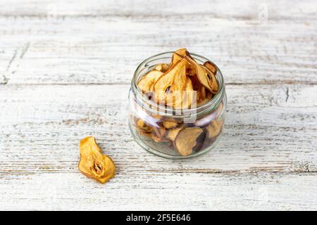 Un mucchio di fette secche di pere in vaso di vetro su sfondo bianco di legno. Patatine di frutta secca. Cibo vegano sano Foto Stock