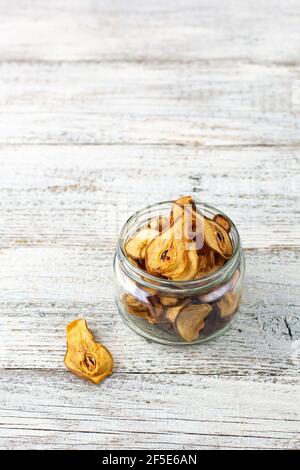 Un mucchio di fette secche di pere in vaso di vetro su sfondo bianco di legno. Patatine di frutta secca. Cibo vegano sano Foto Stock