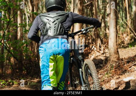 Pedalò teenager latino che cammina lungo il sentiero con la sua montagna pedala attraverso i boschi Foto Stock