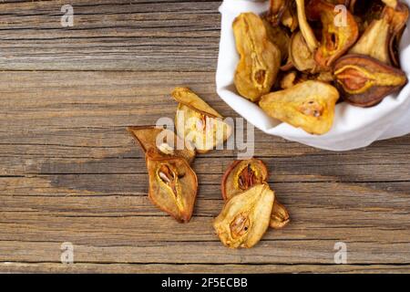 Un mucchio di fette secche di pere in sacchetto bianco su sfondo di legno. Patatine di frutta secca. Cibo vegano sano Foto Stock