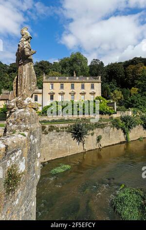 Statua e ponte sul fiume Frome e la classica facciata georgiana del 1730 a sud-ovest di Iford Manor & Gardens; Iford Bradford-on-Avon, Wiltshire, Regno Unito Foto Stock