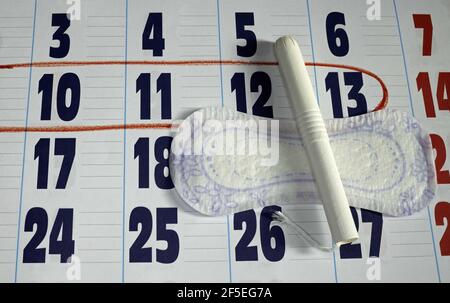 Un cuscino igienico femminile e un tampone su un calendario con giorni selezionati del periodo mestruale Foto Stock