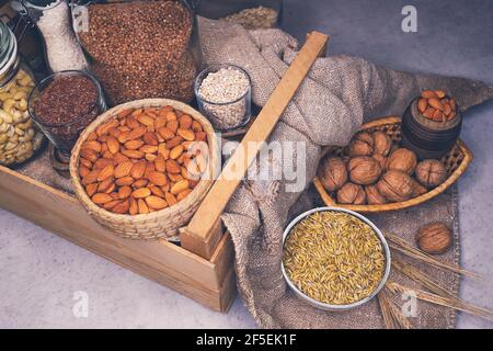 Varietà di cereali e di frutta a guscio in tavola. Noci, mandorle, grani di grano e spighe di mais in lattine e cesti. Fonti alternative di proteine e vitamine Foto Stock