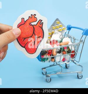 Trattamento o prevenzione di malattie cardiache con varietà di pillole. Matita di cuore umano in mano contro sfondo di molte pillole colorate in groce Foto Stock