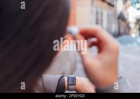 Foto posteriore di una giovane donna che usa auricolari e smart guarda Foto Stock