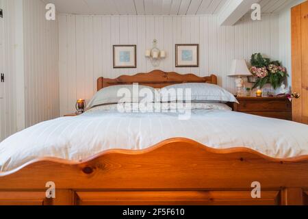 Letto queen size con struttura in legno massello di pino, testiera, pedana nella camera da letto principale al piano superiore con pareti in legno stretto dipinto di bianco all'interno della vecchia casa Foto Stock