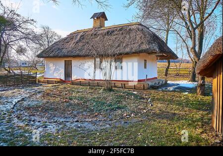 Scena rurale tradizionale per villaggio ucraino - casale hata imbiancato con tetto di paglia, circondato da resti dell'ultima neve di primavera nel bagnato Foto Stock