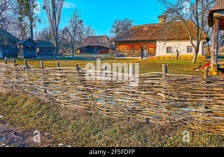 La vista sulla tradizionale fattoria Ucraina attraverso la vecchia recinzione in vimini - le penne in legno, i fienili, i magazzini e la casa di hata imbiancata sono visti nel Foto Stock