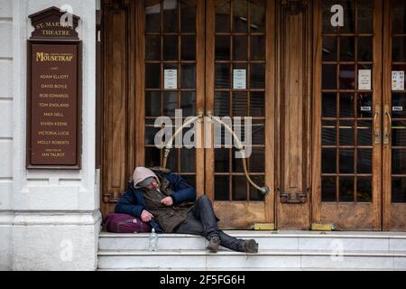 Un uomo senza dimora siede sui gradini del St Martin's Theatre, nel West End di Londra, prima che il blocco del coronavirus realizzò la produzione del Mousetrap. Foto Stock