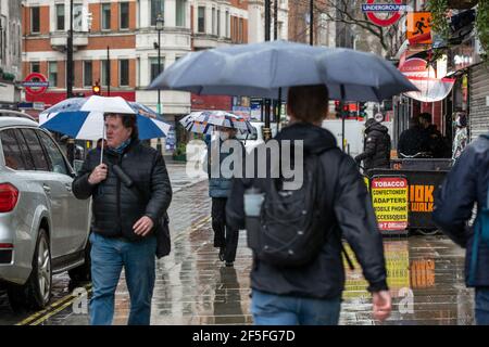 Pedoni che si coprono dalla pioggia tenendo ombrelloni nelle strade deserte del West End di Londra durante le misure di blocco del coronavirus, Inghilterra. Foto Stock