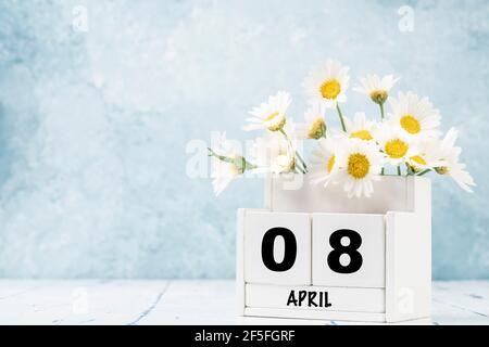 Calendario cubo bianco per aprile decorato con fiori margherita sopra sfondo blu con spazio per la copia Foto Stock