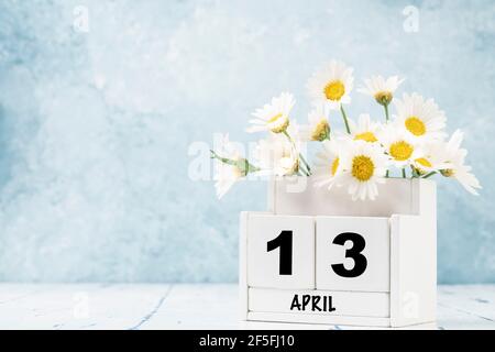 Calendario cubo bianco per aprile decorato con fiori margherita sopra sfondo blu con spazio per la copia Foto Stock