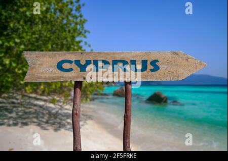 Cipro freccia di legno segno strada contro la spiaggia con sabbia bianca e sfondo di acqua turchese. Viaggio a Cipro Concept. Foto Stock