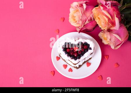 Torta da dessert romantica per San Valentino con rose. Biscotti dolci con crema e cuore rosso per un arredo rosa. Primo piano, spazio per la copia. Foto Stock