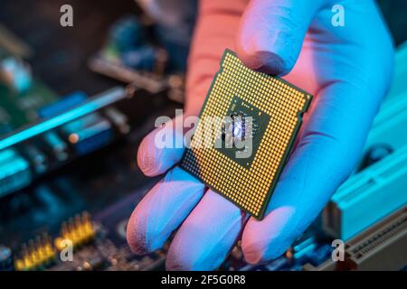 Il guanto del tecnico tiene il chip della CPU sullo sfondo della scheda madre. Concetto di microelettronica hardware ad alta tecnologia Foto Stock
