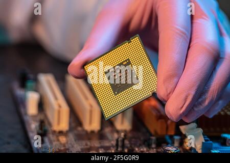 Il guanto del tecnico tiene il chip della CPU sullo sfondo della scheda madre. Concetto di microelettronica hardware ad alta tecnologia Foto Stock
