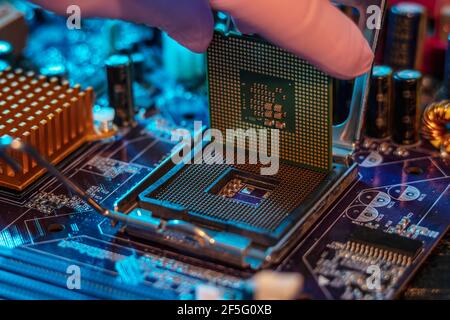 Il guanto del tecnico tiene il chip della CPU sullo sfondo della scheda madre. Concetto di microelettronica hardware ad alta tecnologia Foto Stock