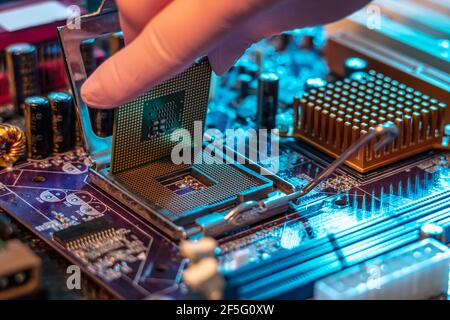 Il guanto del tecnico tiene il chip della CPU sullo sfondo della scheda madre. Concetto di microelettronica hardware ad alta tecnologia Foto Stock