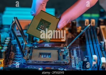 Il guanto del tecnico tiene il chip della CPU sullo sfondo della scheda madre. Concetto di microelettronica hardware ad alta tecnologia Foto Stock