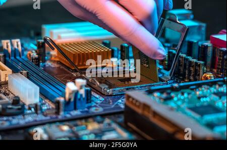 Il guanto del tecnico tiene il chip della CPU sullo sfondo della scheda madre. Concetto di microelettronica hardware ad alta tecnologia Foto Stock