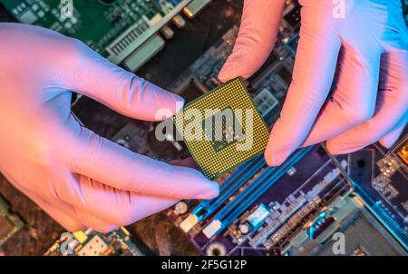 Il guanto del tecnico tiene il chip della CPU sullo sfondo della scheda madre. Concetto di microelettronica hardware ad alta tecnologia Foto Stock