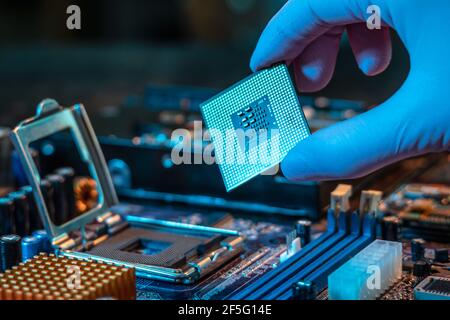Il guanto del tecnico tiene il chip della CPU sullo sfondo della scheda madre. Concetto di microelettronica hardware ad alta tecnologia Foto Stock