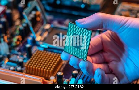 Il guanto del tecnico tiene il chip della CPU sullo sfondo della scheda madre. Concetto di microelettronica hardware ad alta tecnologia Foto Stock