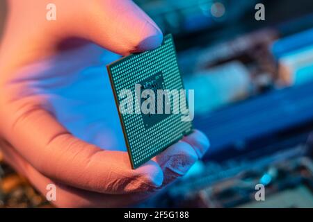 Il guanto del tecnico tiene il chip della CPU sullo sfondo della scheda madre. Concetto di microelettronica hardware ad alta tecnologia Foto Stock