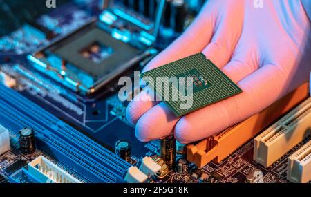 Il guanto del tecnico tiene il chip della CPU sullo sfondo della scheda madre. Concetto di microelettronica hardware ad alta tecnologia Foto Stock