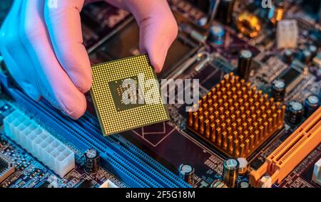 Il guanto del tecnico tiene il chip della CPU sullo sfondo della scheda madre. Concetto di microelettronica hardware ad alta tecnologia Foto Stock