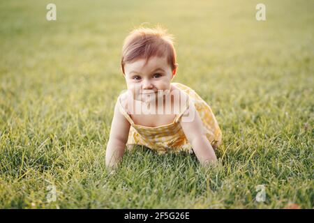 Carina bambina strisciata a terra in parco all'aperto. Adorabile bimbo che esplora il mondo di studiare. Sviluppo fisico sano. Ki divertente Foto Stock