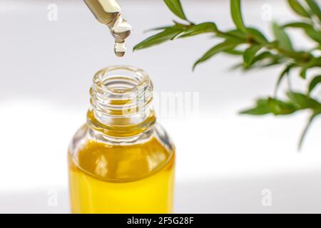 Primo piano goccia di olio essenziale o organico giallo in una pipetta di vetro, sopra una bottiglia Foto Stock